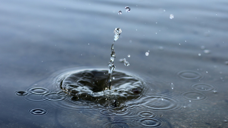 静かな水面に水滴が落ちて王冠状のしぶきが立ち、同心円の波紋が広がっている様子