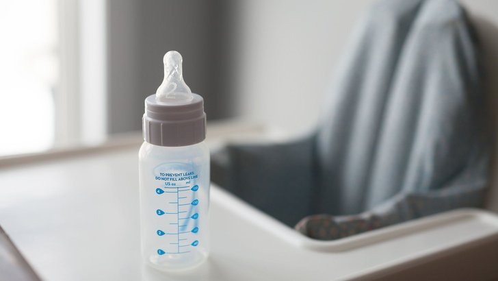 ベビーチェアのトレイに置かれた目盛り付きの哺乳瓶