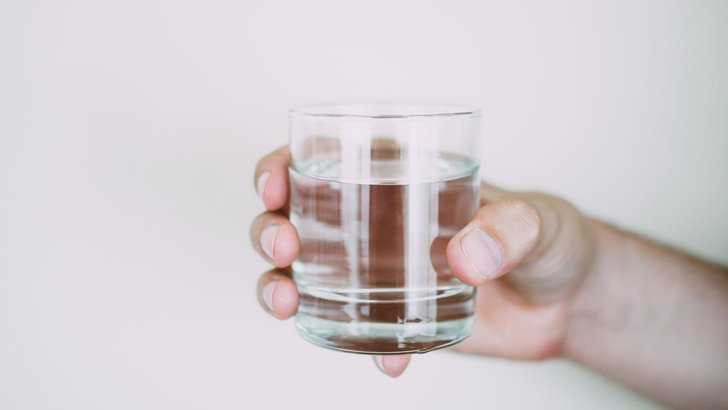 明るい光のなかで、水の入った透明なグラスを手に持っているところ