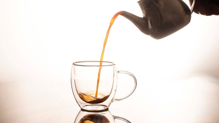 ティーポットからガラスのカップに紅茶を注いでいるところ