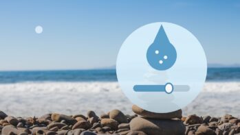 海辺の積み石の写真を背景にミネラルの粒が入った水滴と硬度の横スライダーを描いたイラスト（硬度とは？の記事）