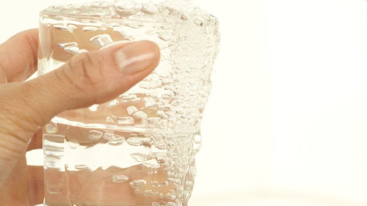 明るい光のなかで、水の入った透明なグラスを手に持っているところ