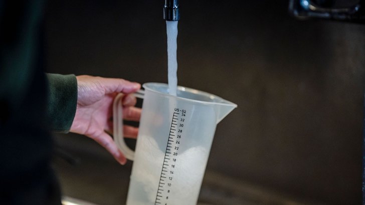 キッチンの蛇口から計量カップに水道水を注いでいる手元