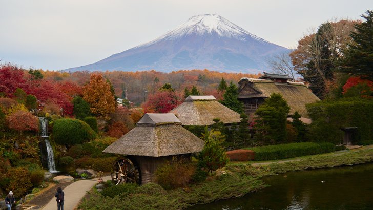 紅葉の忍野八海。茅葺屋根の水車小屋と池、奥に冠雪した富士山