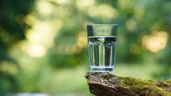 緑を背景に置かれた透明な水のグラス（ウォーターサーバー10社比較のアイキャッチ）