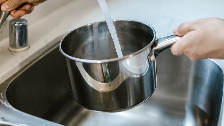 キッチンの水栓から、手に持った容器に水道水を注いでいるところ