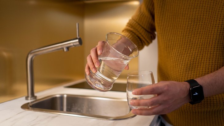 明るいキッチンのシンクの前で、グラスに水を注いでいる手元