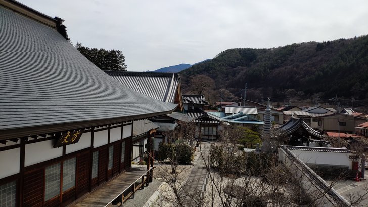 木曽福島の長福寺の本堂の屋根越しに、谷に沿って並ぶ町の家々と山が見える
