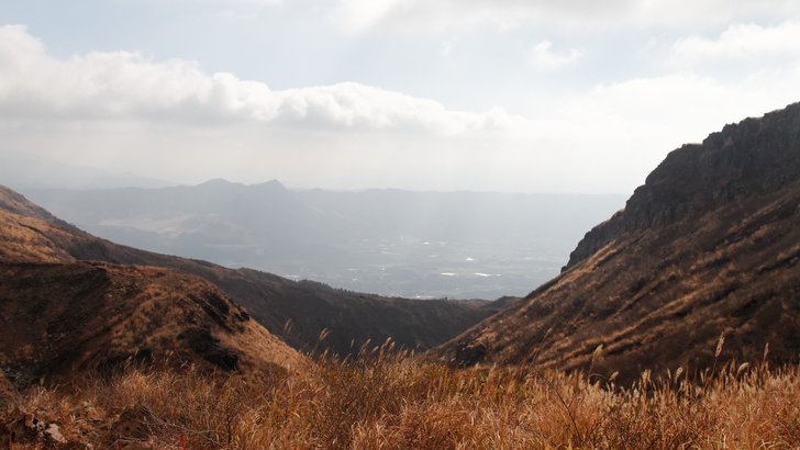 阿蘇の中央火口丘から南を望む。ススキの斜面の先に南郷谷の平地と外輪山の南壁が連なる