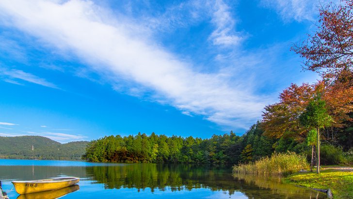 秋の青木湖。澄んだ湖面に紅葉と針葉樹が映り、岸に小舟が浮かぶ