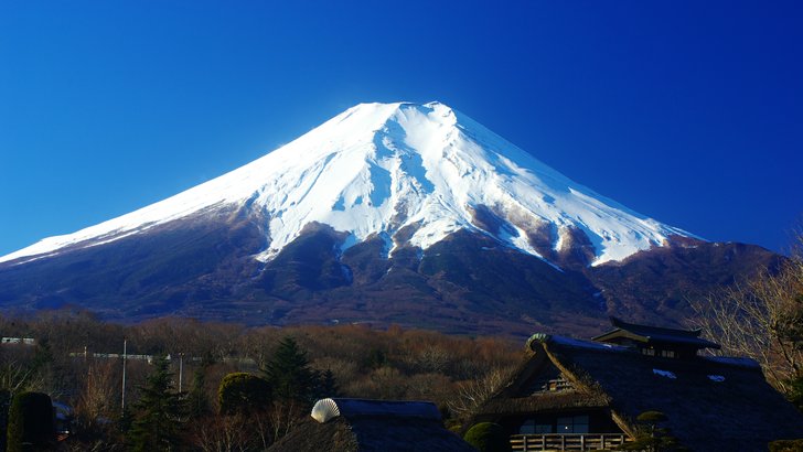 忍野八海から望む冠雪した富士山と青空。手前に茅葺屋根