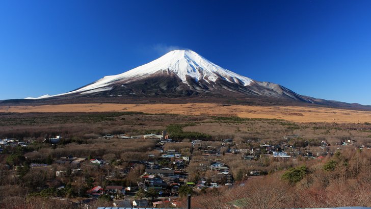 山中湖村の集落の屋根越しに見る冬の富士山。裾野の草原が茶色に広がる