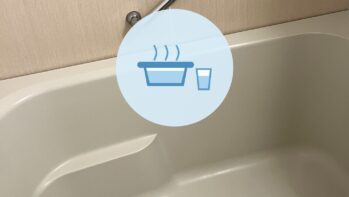 湯気の立つ浴槽と水の入ったコップのアイコン。背景は浴室の壁と手すりと浴槽